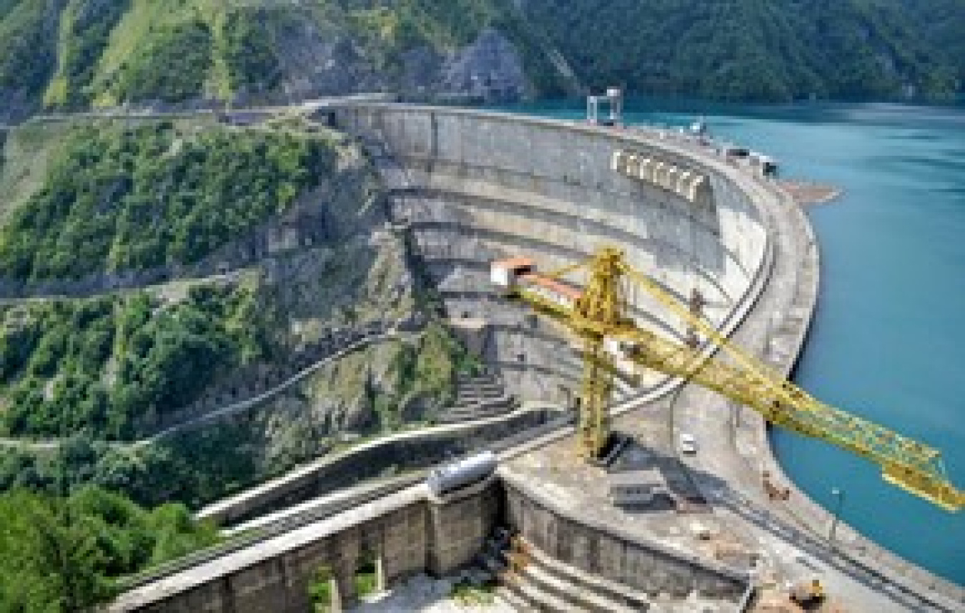 Hydropower dam with greenery surrounding it and mountains in the background.