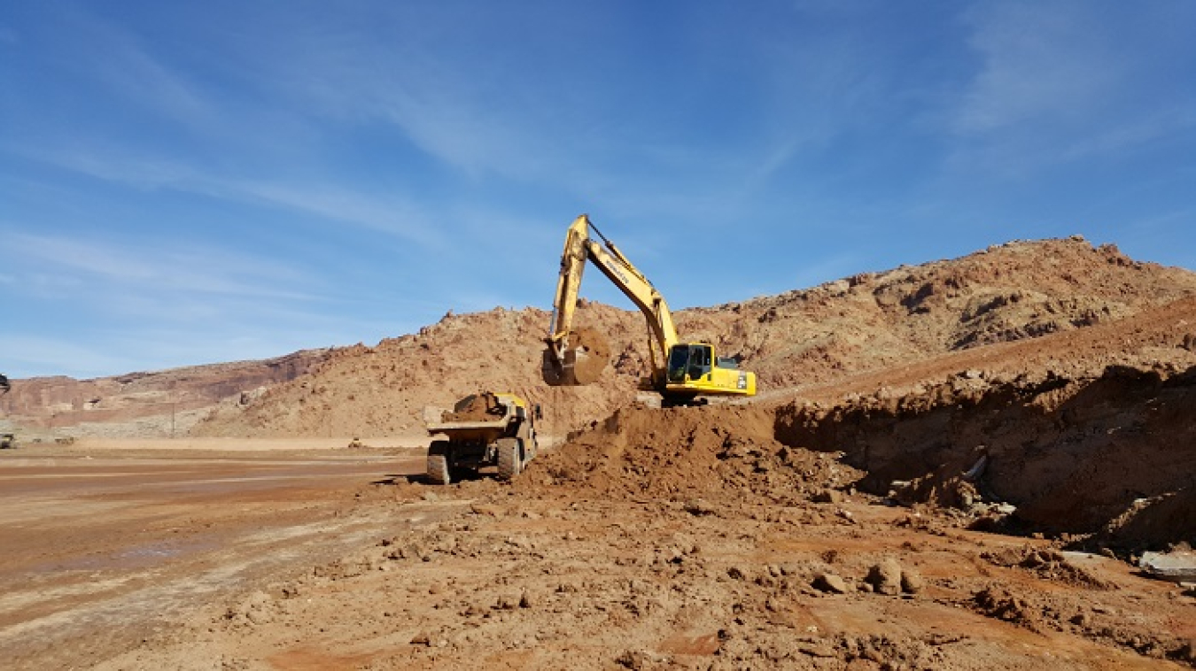 Workers at the Moab Uranium Mill Tailings Remedial Action Project site use an excavator to load uranium mill tailings, a sand-like material that remains from processing uranium ore, into a haul truck for transport for moisture conditioning prior to loading into containers for disposal.
