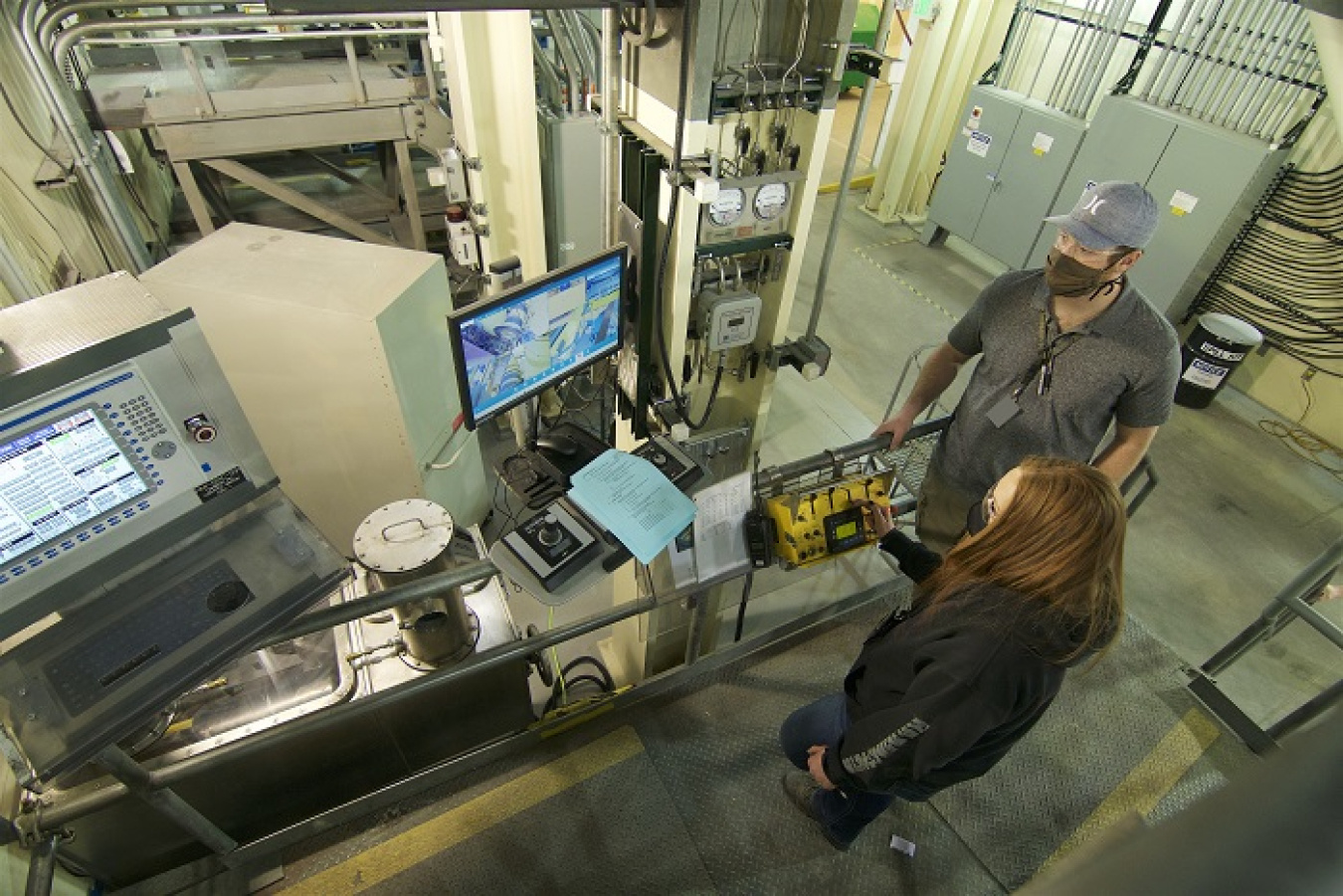 Integrated Waste Treatment Unit (IWTU) operator Samantha Phillips operates a crane at the facility at DOE's Idaho National Laboratory Site while Trevor Clark, also an IWTU operator, observes.