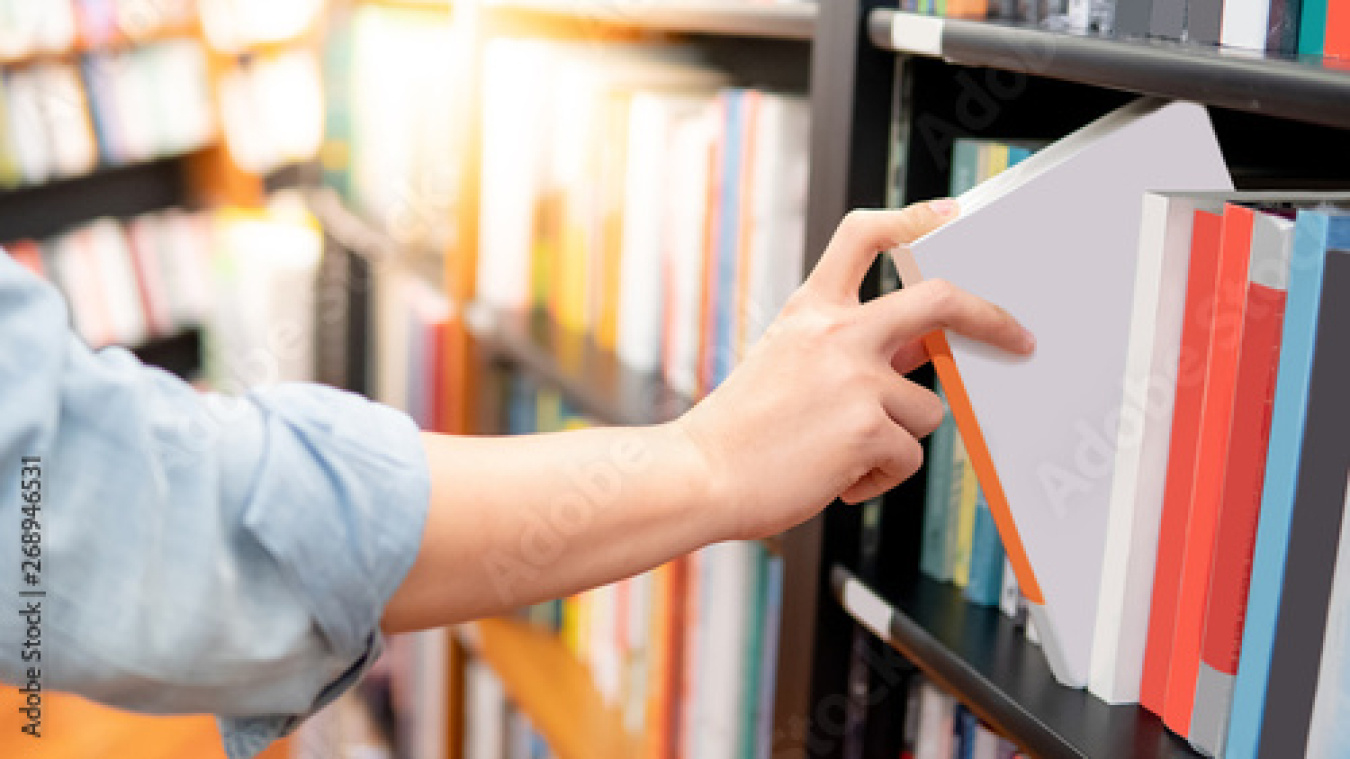 Male hand choosing and picking book from wooden bookshelf in bookstore or library.