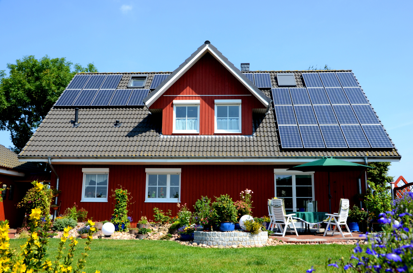 Exterior of a house with solar panels on it and a lawn in front of it with lawn furniture and various shrubs.