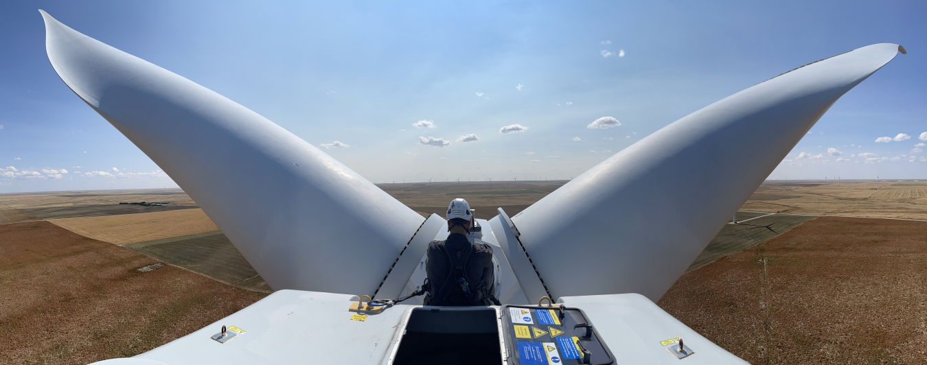Panoramic view from the top of a wind turbine, taken from behind a person in a hardhat.