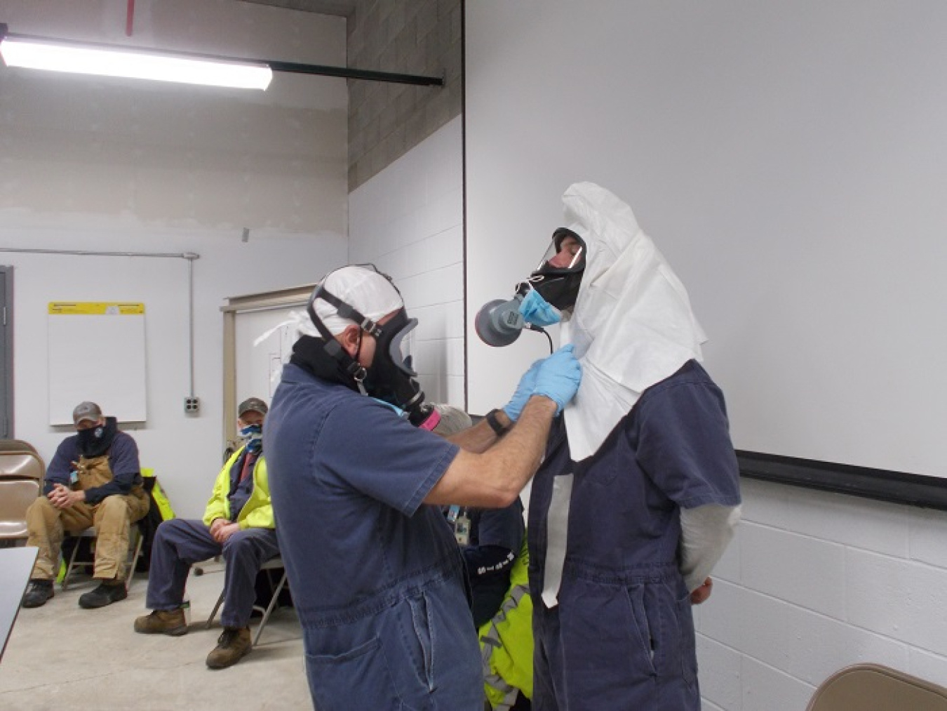 CH2M HILL BWXT West Valley Facility Disposition Supervisor Tim Wittmeyer, left, and co-worker Mike Sexton demonstrate donning and doffing personal protective equipment during a mock-up session at the West Valley Demonstration Project.