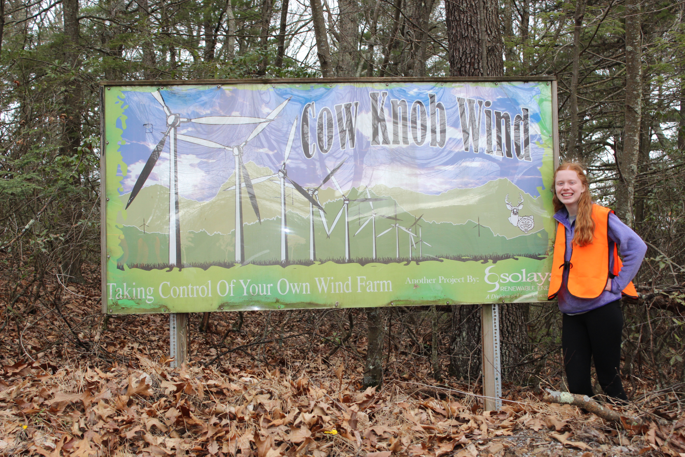 Graduate Jamie Mears stands next to a sign in the woods.