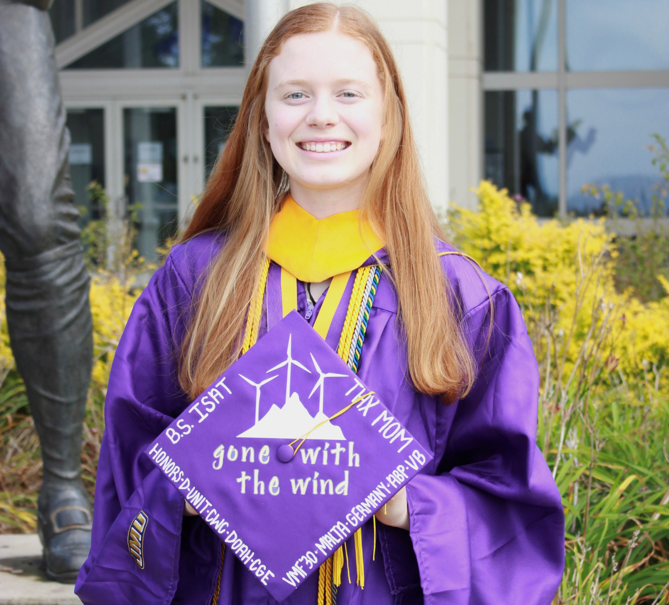 Woman stands smiling with her cap and gown. 