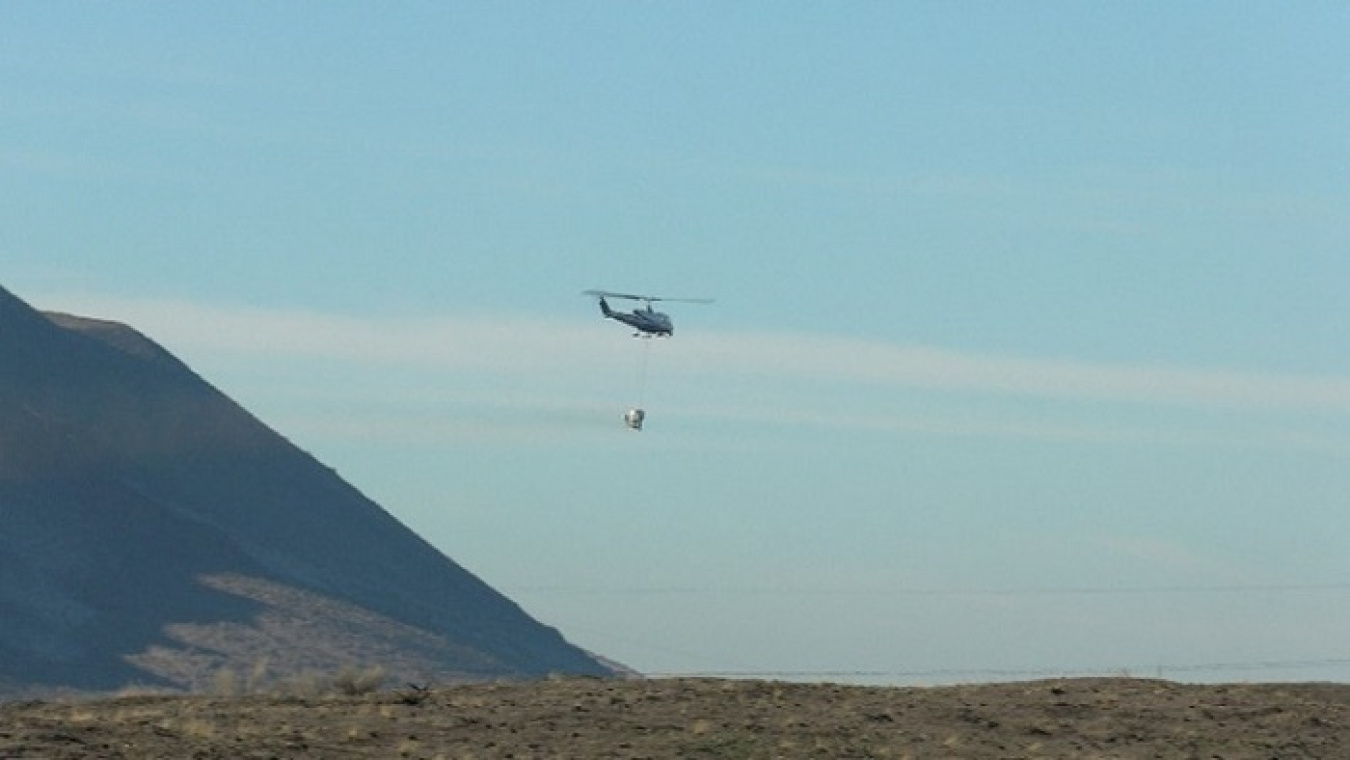 A helicopter drops a bucket of native grass and shrub seed on portions of the Hanford Site that burned during the Gable Mountain fire in June last year. The seed will restore critical habitat and help prevent erosion.