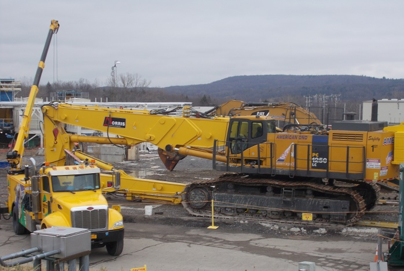 Workers at the West Valley Demonstration Project install a long-reach arm on a large excavator that will be used for the demolition of the Main Plant Process Building.
