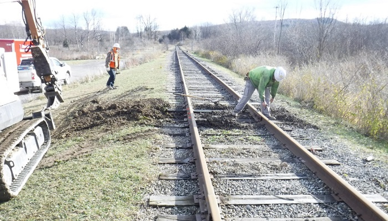 Using a small excavator, workers replace railroad ties along a track within the West Valley Demonstration Project used to ship waste offsite for disposal.