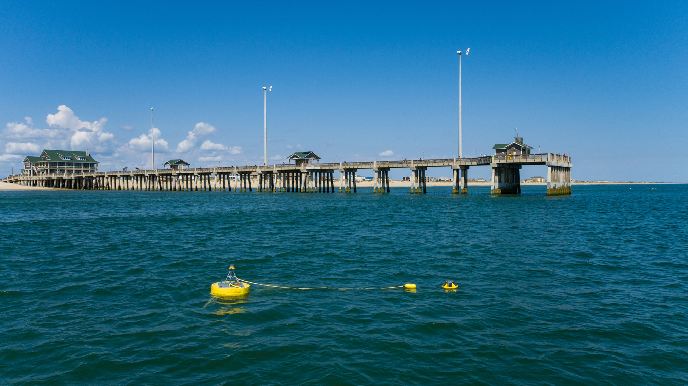 A yellow buoy floats in the ocean water next to a fishing pier.