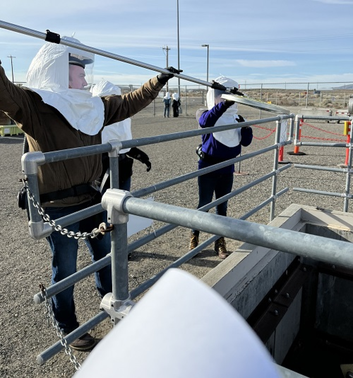 Employees in supplied air maneuver long-reach tools during an activity to simulate removing items from a pit. The training is conducted by Hanford’s Volpentest HAMMER Federal Training Center.