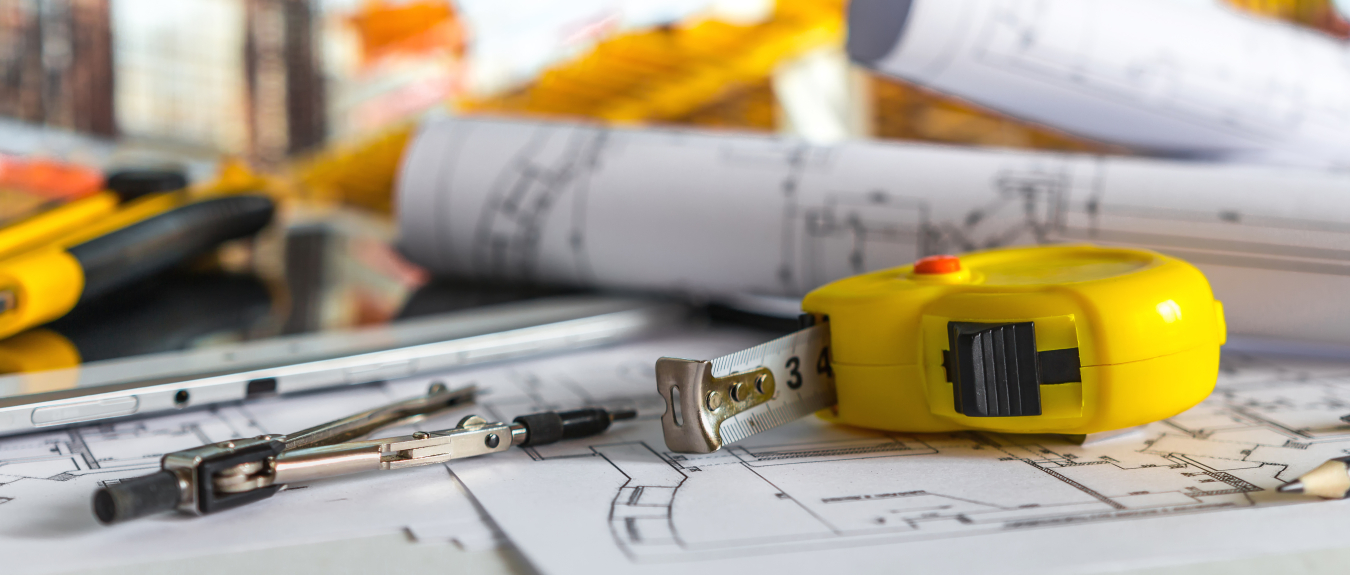 A building contractor's tape measure, blueprints and other tools lying on a table.