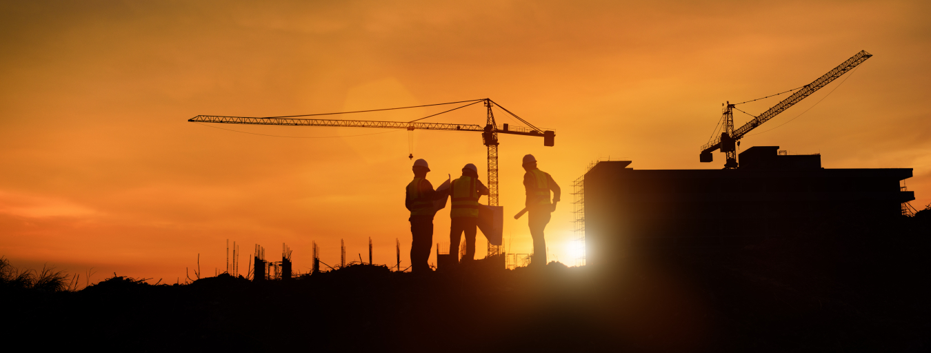 Silhouette image of engineers doing construction work with a tower crane and a setting sun in the background.