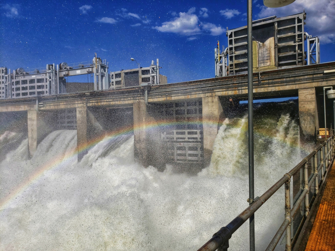 A rainbow forms across a waterfall created by a dam.