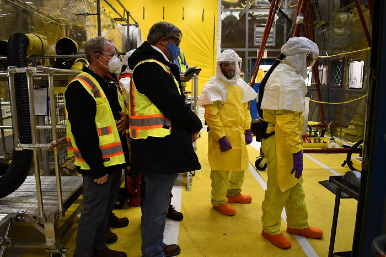 EM Senior Advisor William “Ike” White, far left, observes preparations underway to implement a processing line that allows the removal of liquids from drums containing transuranic (TRU) waste.