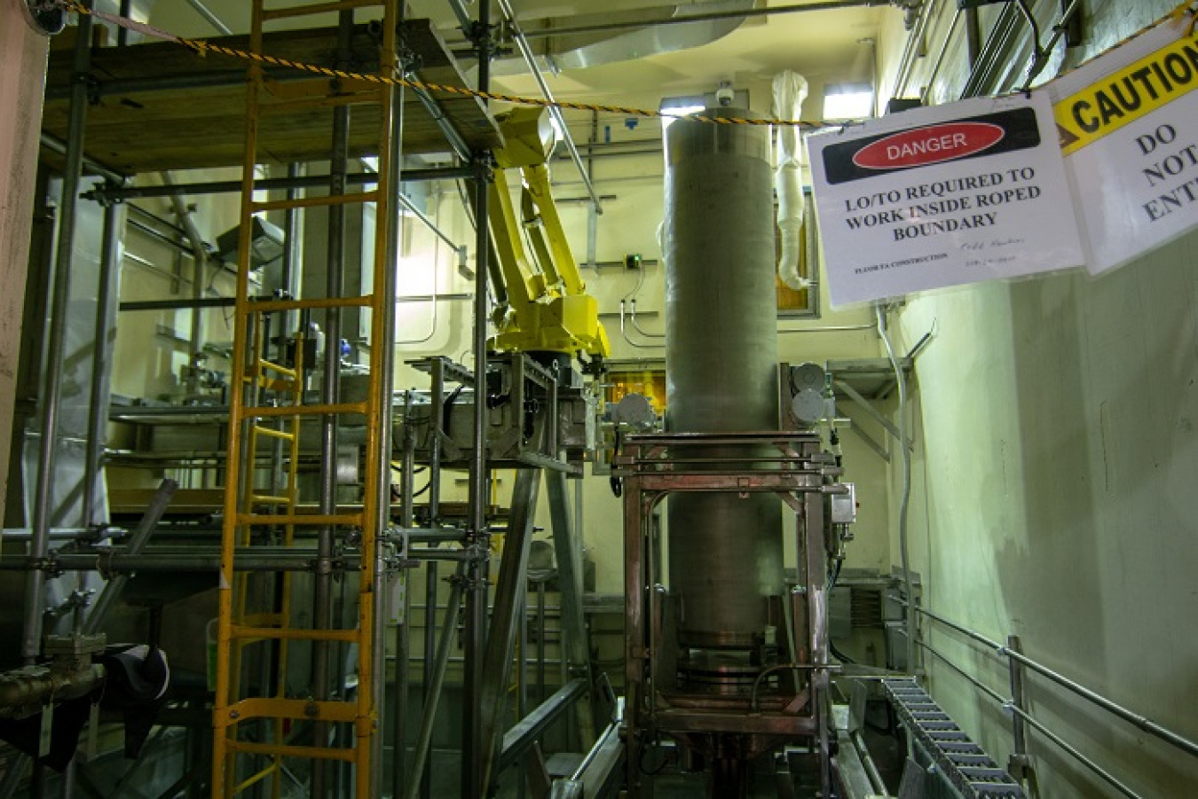 A robotic arm, shown in yellow at center, undergoes testing at the Integrated Waste Treatment Unit at DOE's Idaho National Laboratory Site to remove contamination from stainless steel canisters containing a treated waste product.