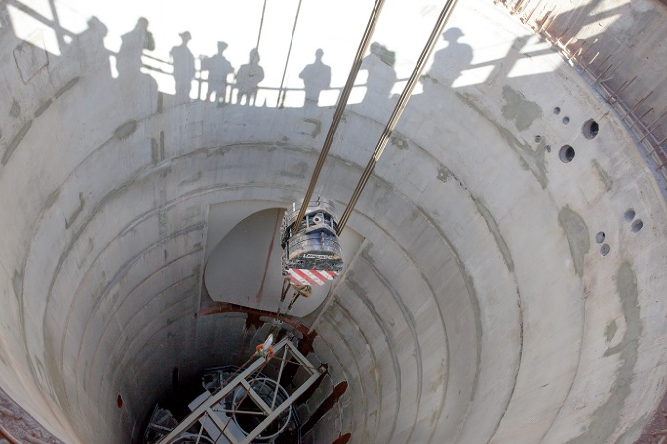 As workers line the rails to watch, the Galloway work platform comes to rest on supports 116 feet down in the Waste Isolation Pilot Plant’s utility shaft being constructed. The work platform and its excavation tools will eventually be suspended on cables running from hoists and over the top of a metal frame known as a headframe now being constructed over the shaft.