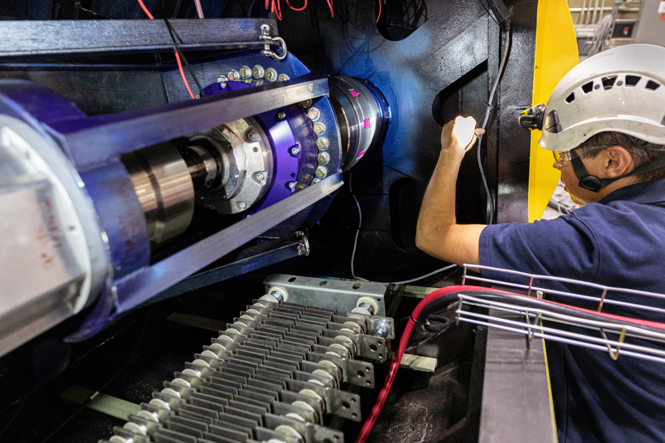 A researcher shines a light on the end of an autonomous offshore power system, a large, blue, cylindrical machine.