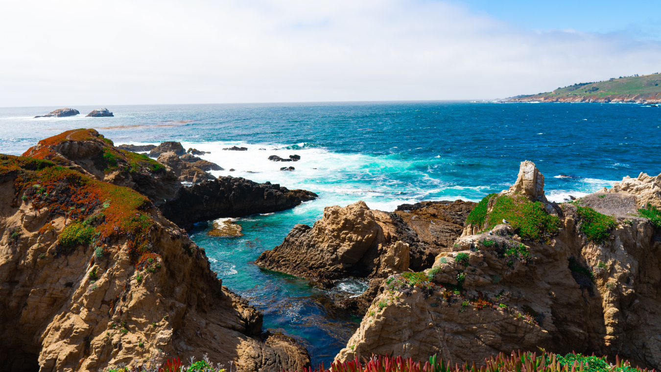 Ocean waves flow into a channel between tall, craggy rocks along a coastline.