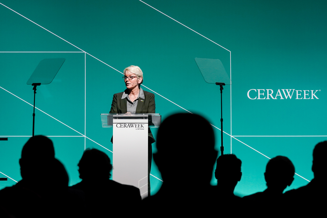 Secretary Granholm stands in front of a white podium and speaks to a crowd in front of a teal background that incorporates the white CERAWeek logo.