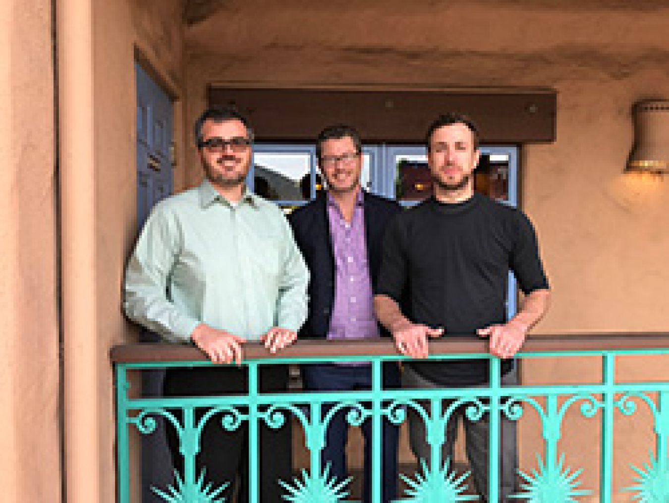 Three men smiling while standing outside.