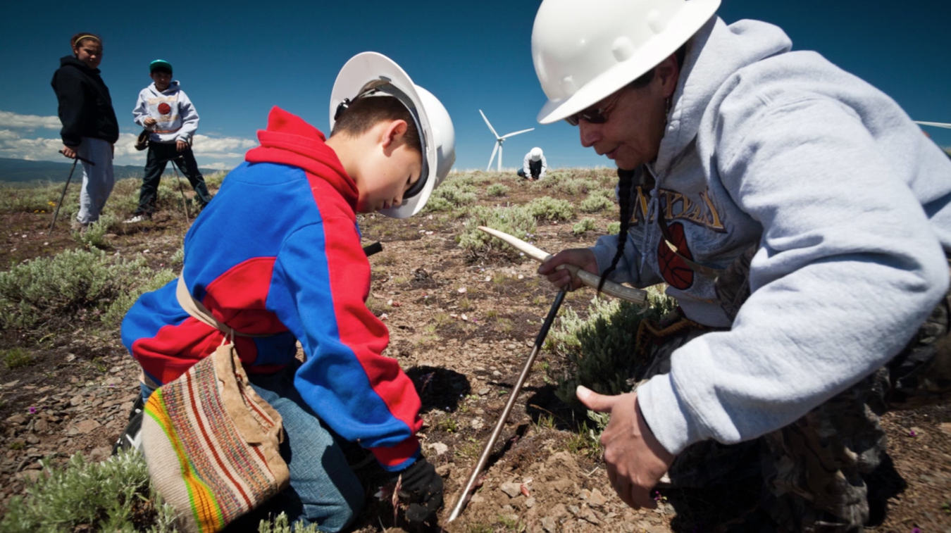 a photo of several people working in a field, with a wind turbine in the background.