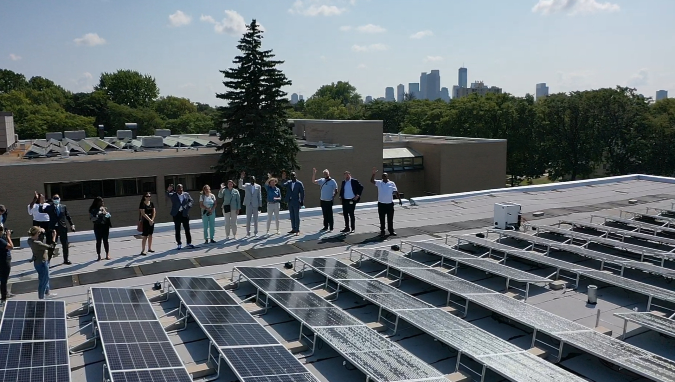 A photo of people standing on a roof next to a solar array in Minneapolis, MN