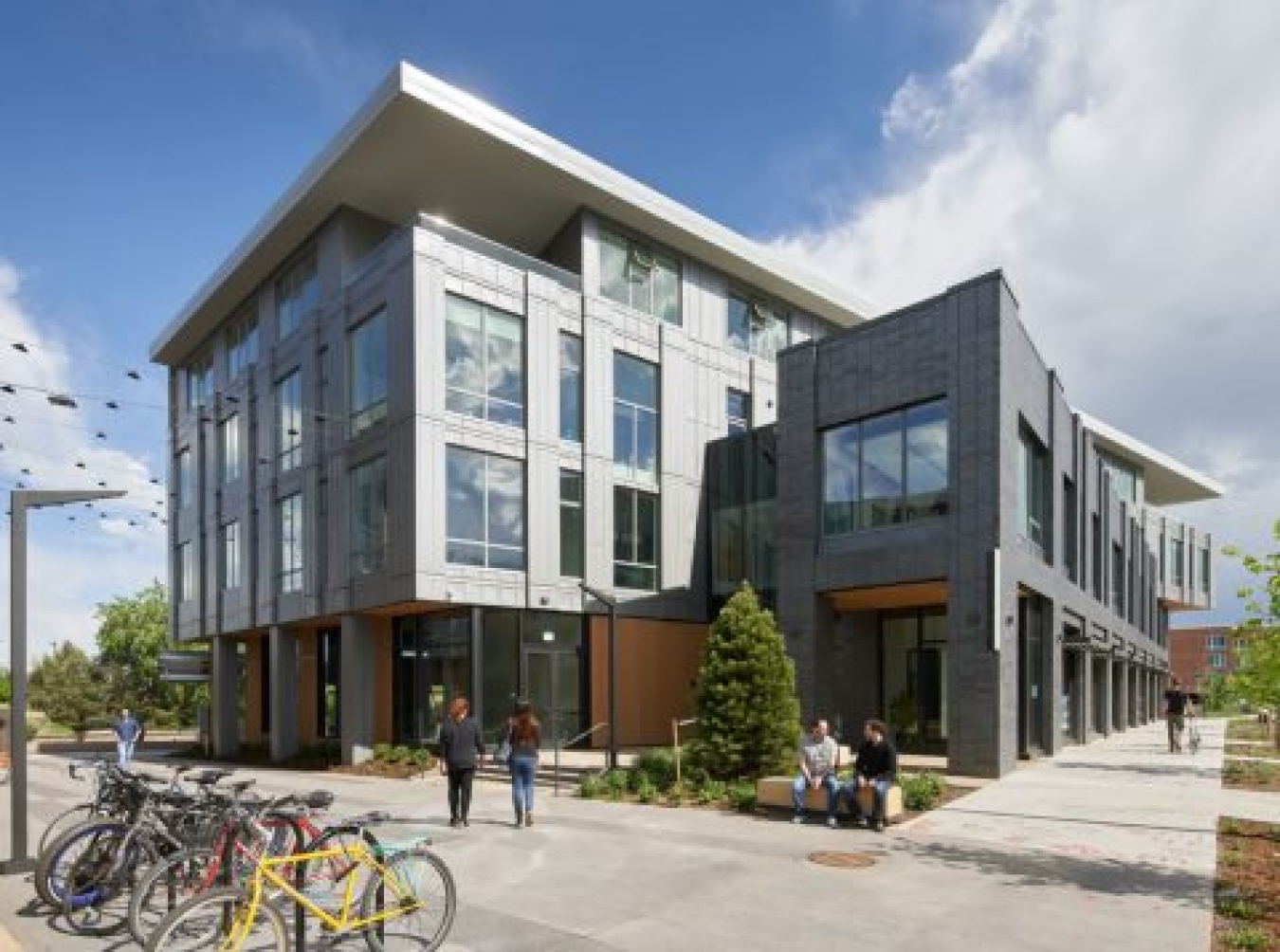 Exterior of the Boulder Commons building, with two people standing in front of it, as well as a bicycle rack.