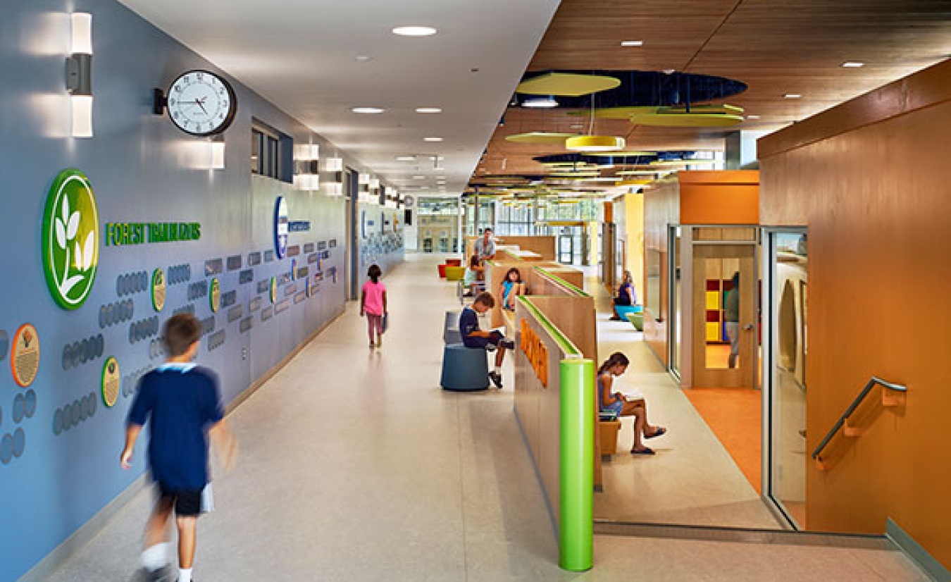 The corridor of an elementary school, with children walking or sitting and reading.