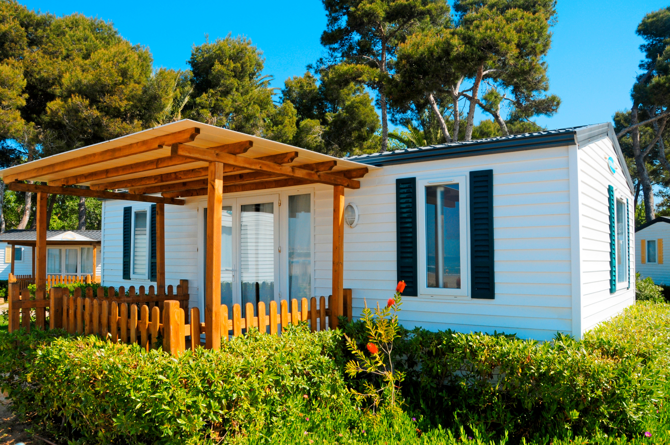 The exterior of a manufactured house, with a wooden gazebo-type structure attached to it.