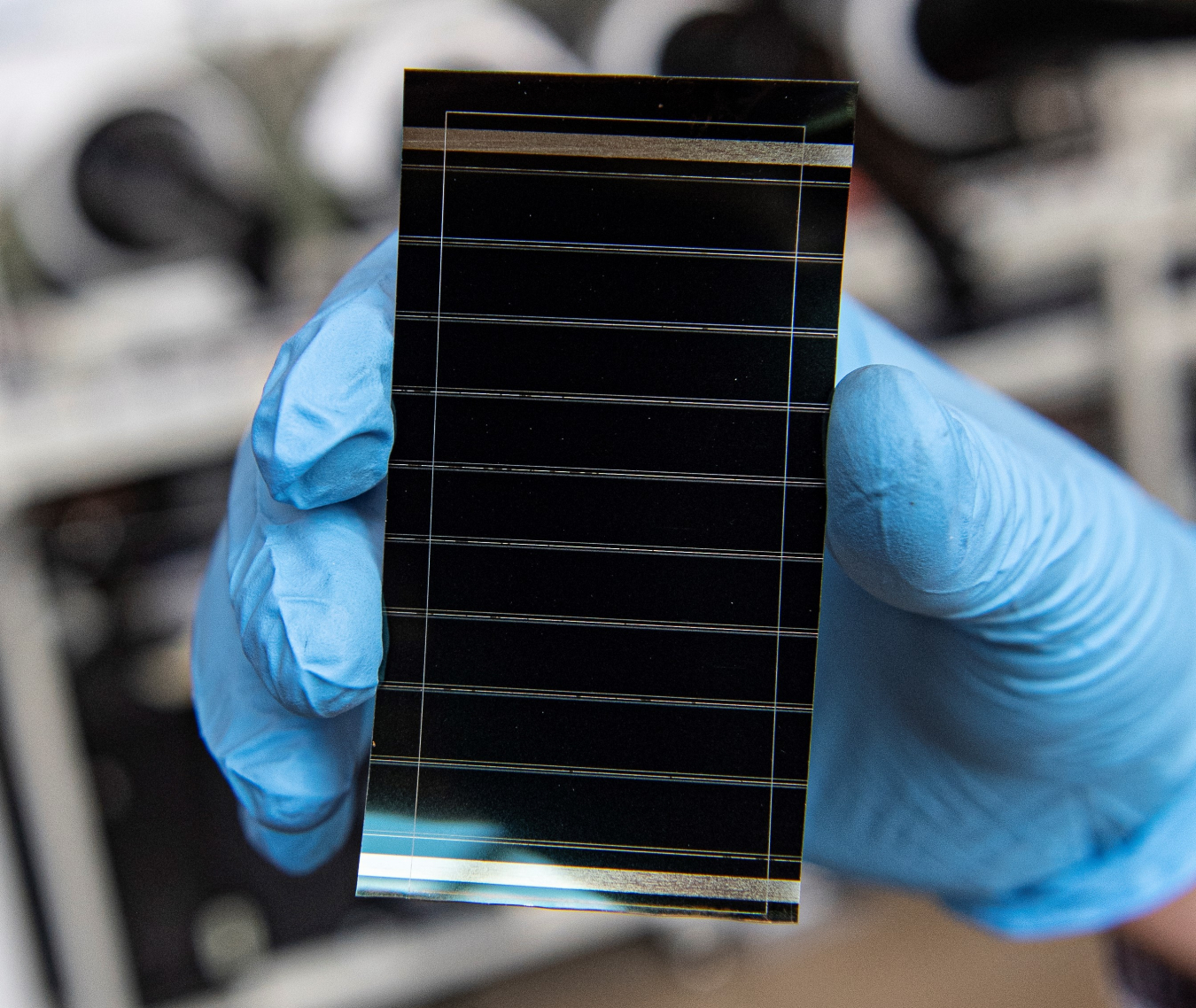 Photo of a gloved hand holding a perovskite solar cell