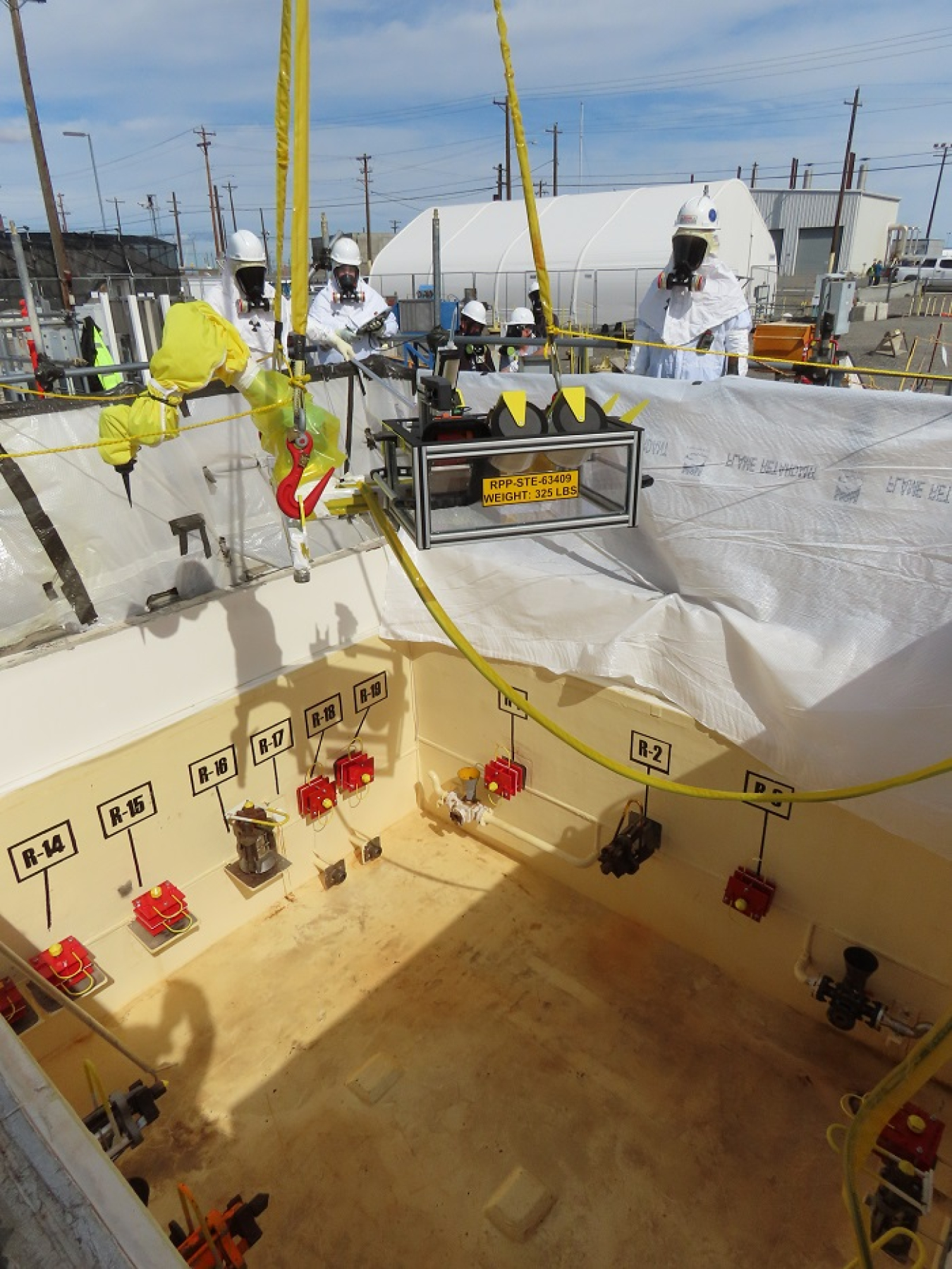 Workers with EM Office of River Protection contractor Washington River Protection Solutions stand at ground level as a coating repair cobot, or collaborative robot, is lowered into a valve pit to conduct repairs at the Hanford Site.