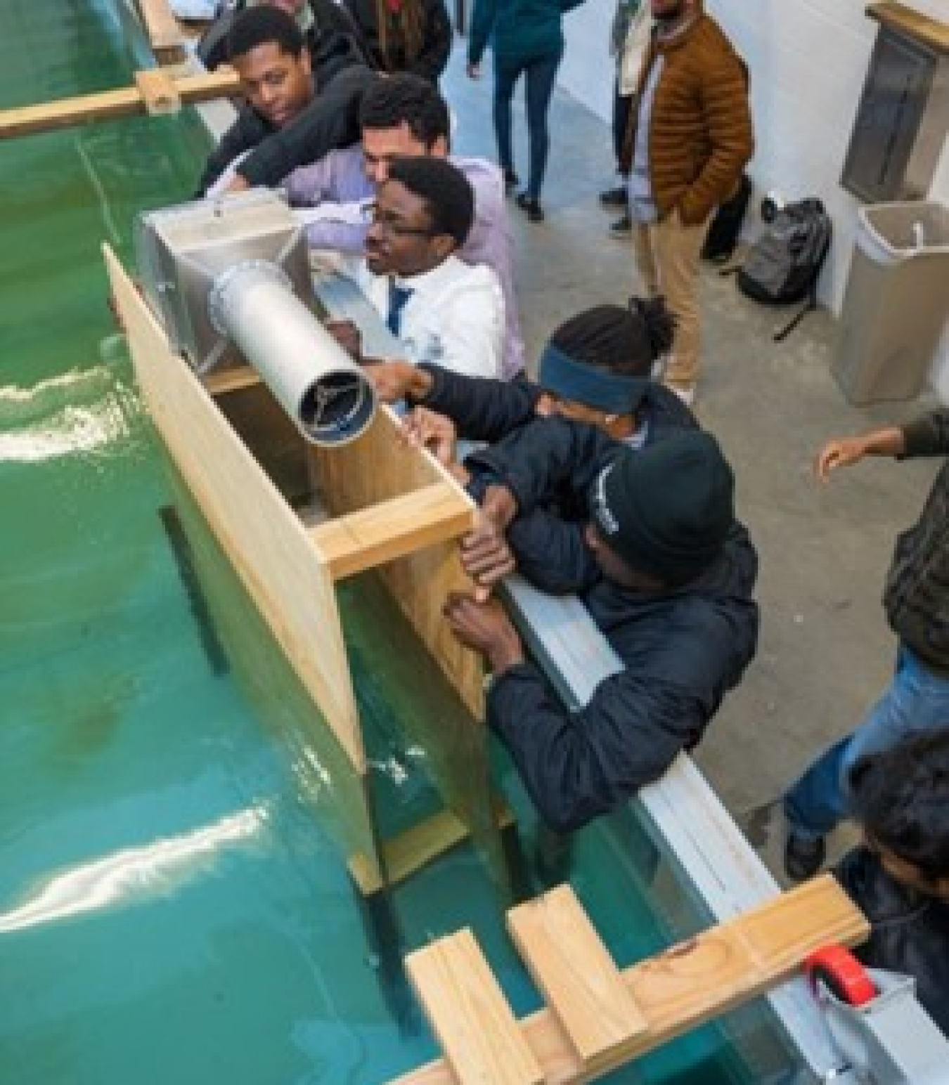 A group of people leaning on a tank full of water holding onto a metal contraption.