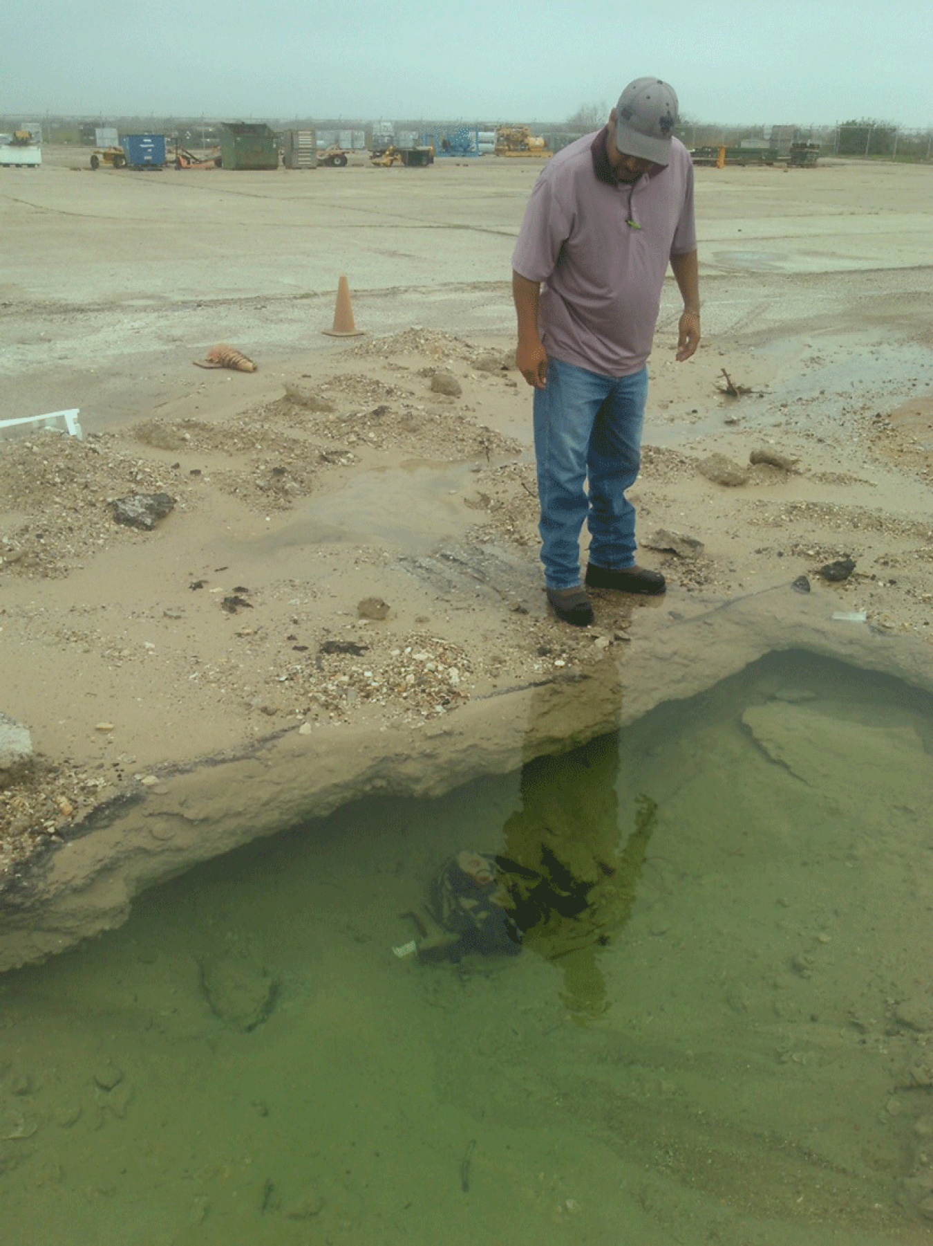 A man standing on a beach looking down at a submerged water pipeline.