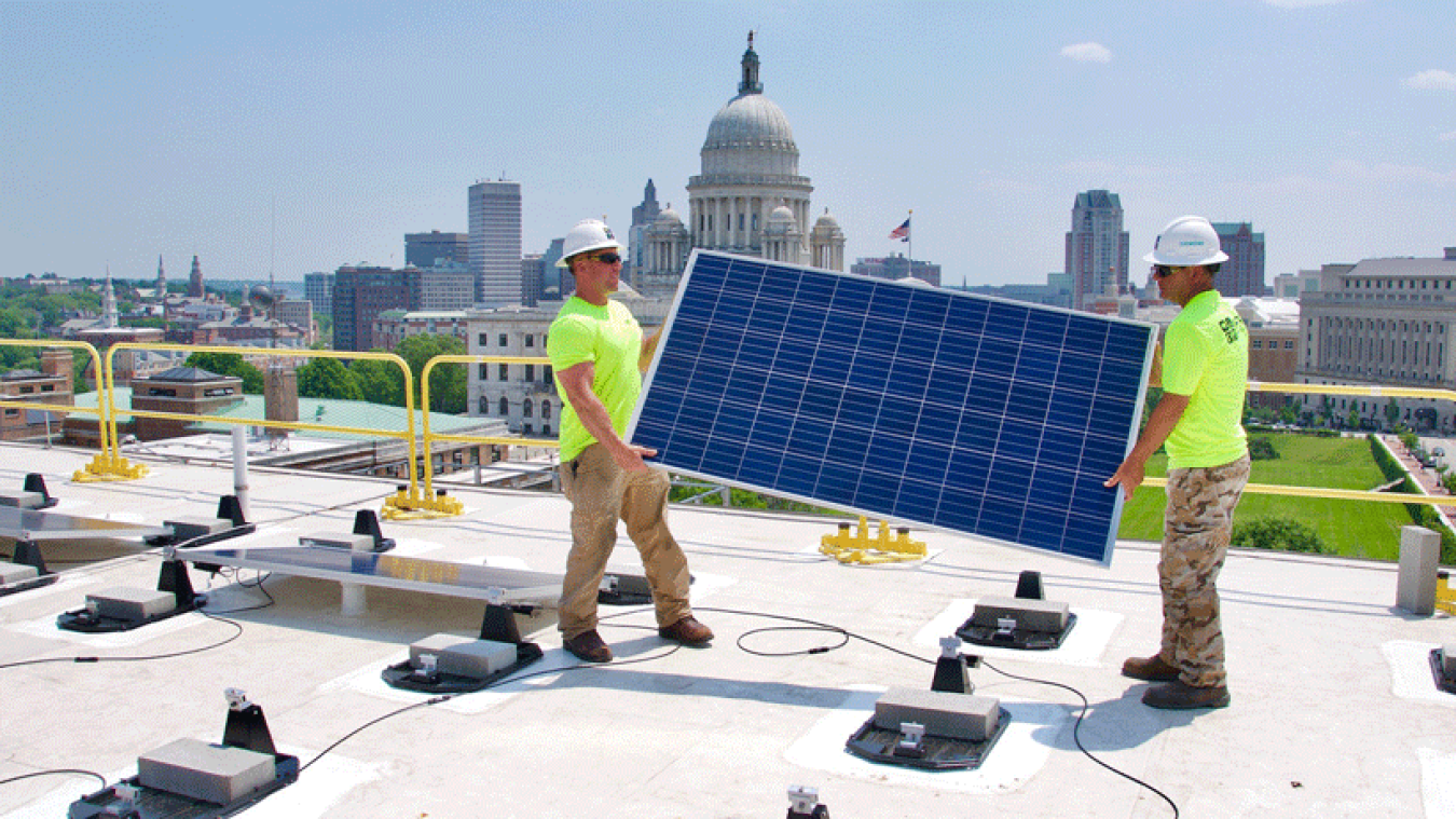 Two men installing solar panels on the roof of a government building in Rhode Island.