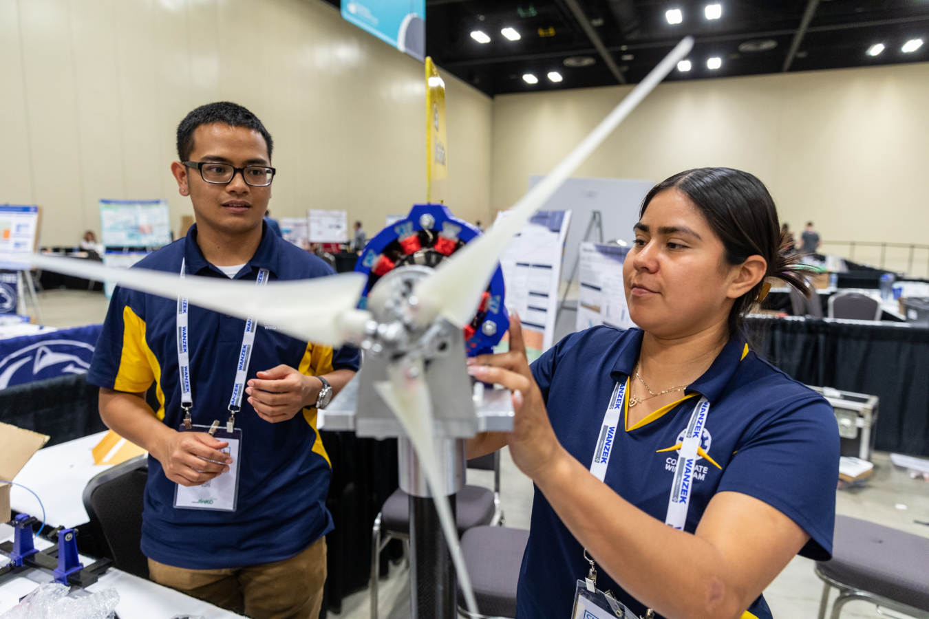 Two young people work on a small prototype wind turbine in an exhibition hall.