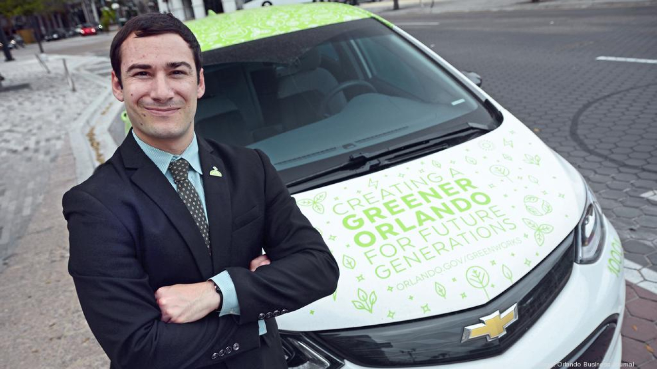 Chris Castro, former director of sustainability and resilience for the city of Orlando, poses in front of an electric vehicle.