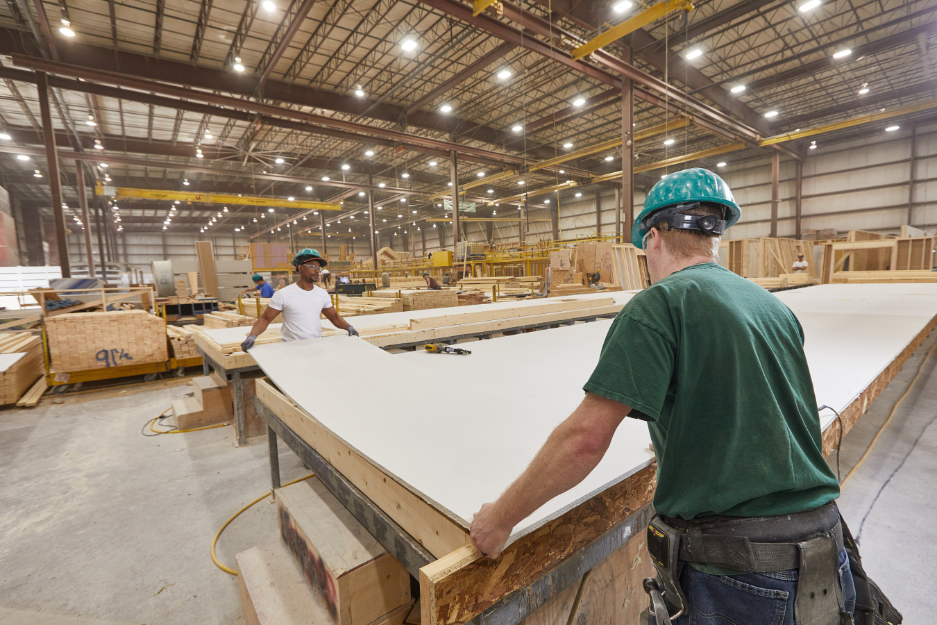 Two men working with large sheets of building materials in a warehouse.