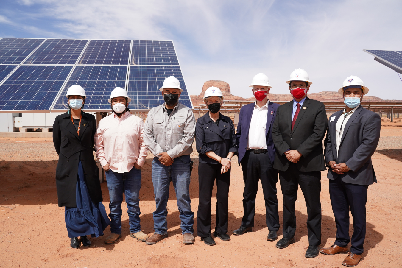 Group of people with hardhats in front of solar panels.