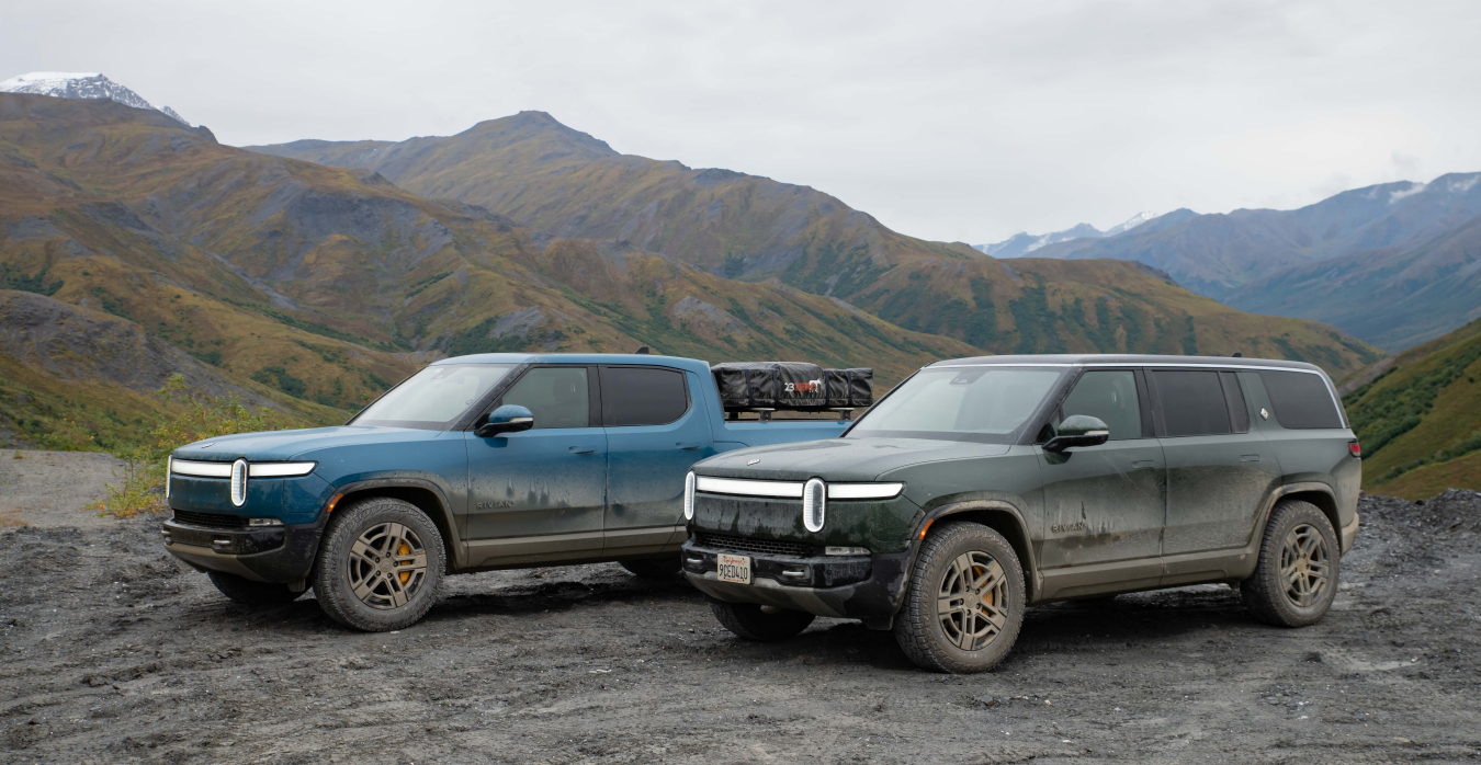 Two Rivian SUVs parked along the Dalton Highway with mountain peaks in the background.