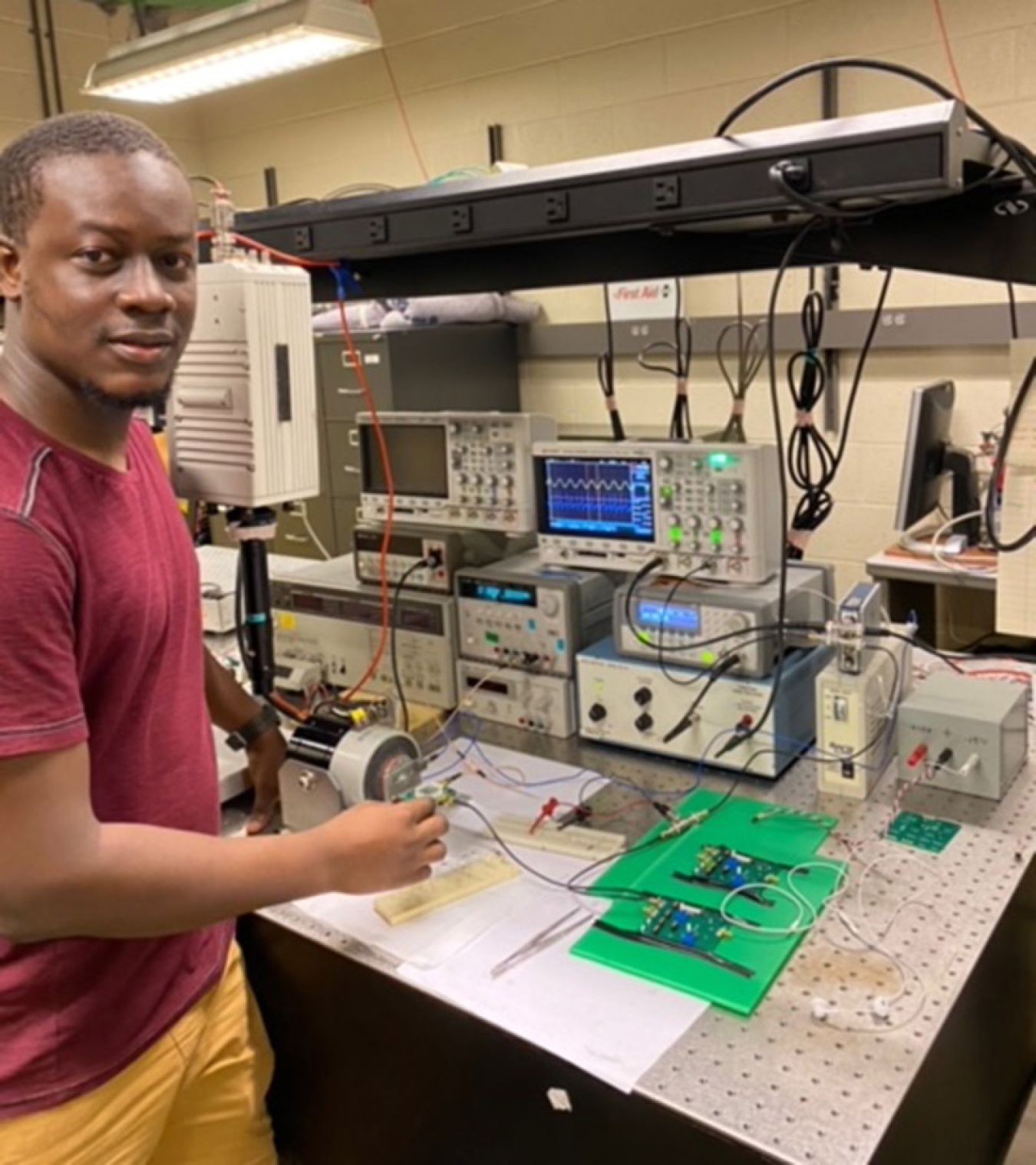 Habilou Ouro-Koura standing at a lab bench, which is covered with electronics and papers