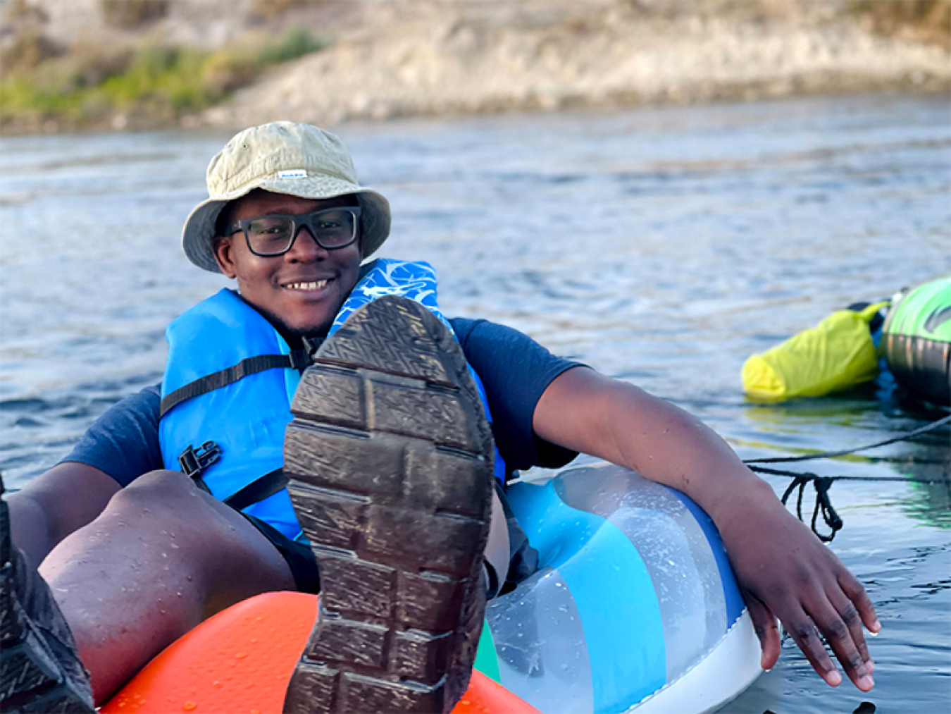 Habilou Ouro-Koura wearing a life jacket as he floats on an inflatable tube in a river
