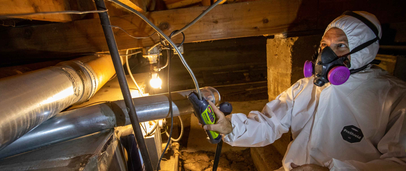 Weatherization worker in a suit and mask working under a house.