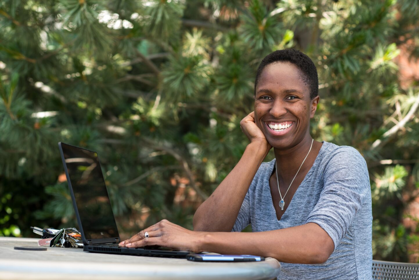 Dr. Charmayne Lonergan sits at a desk outside with her laptop.