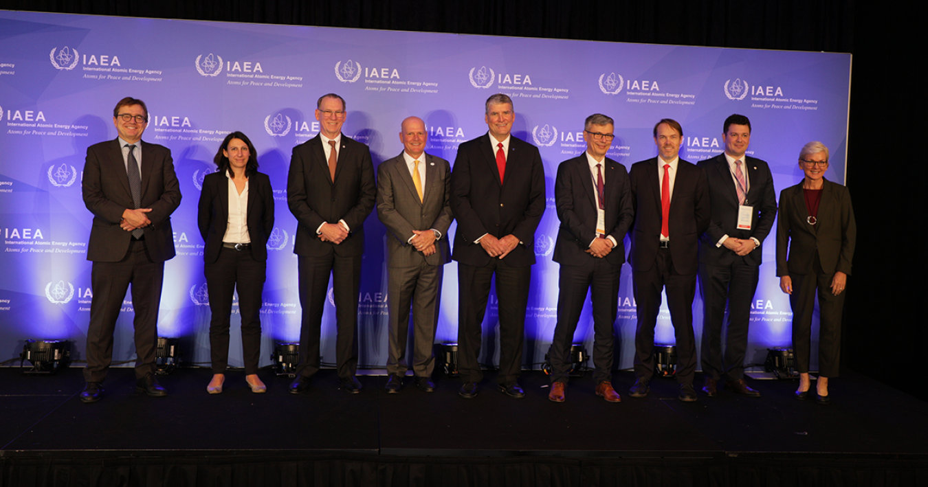 A row of people in suits standing on a stage in front of an audience.