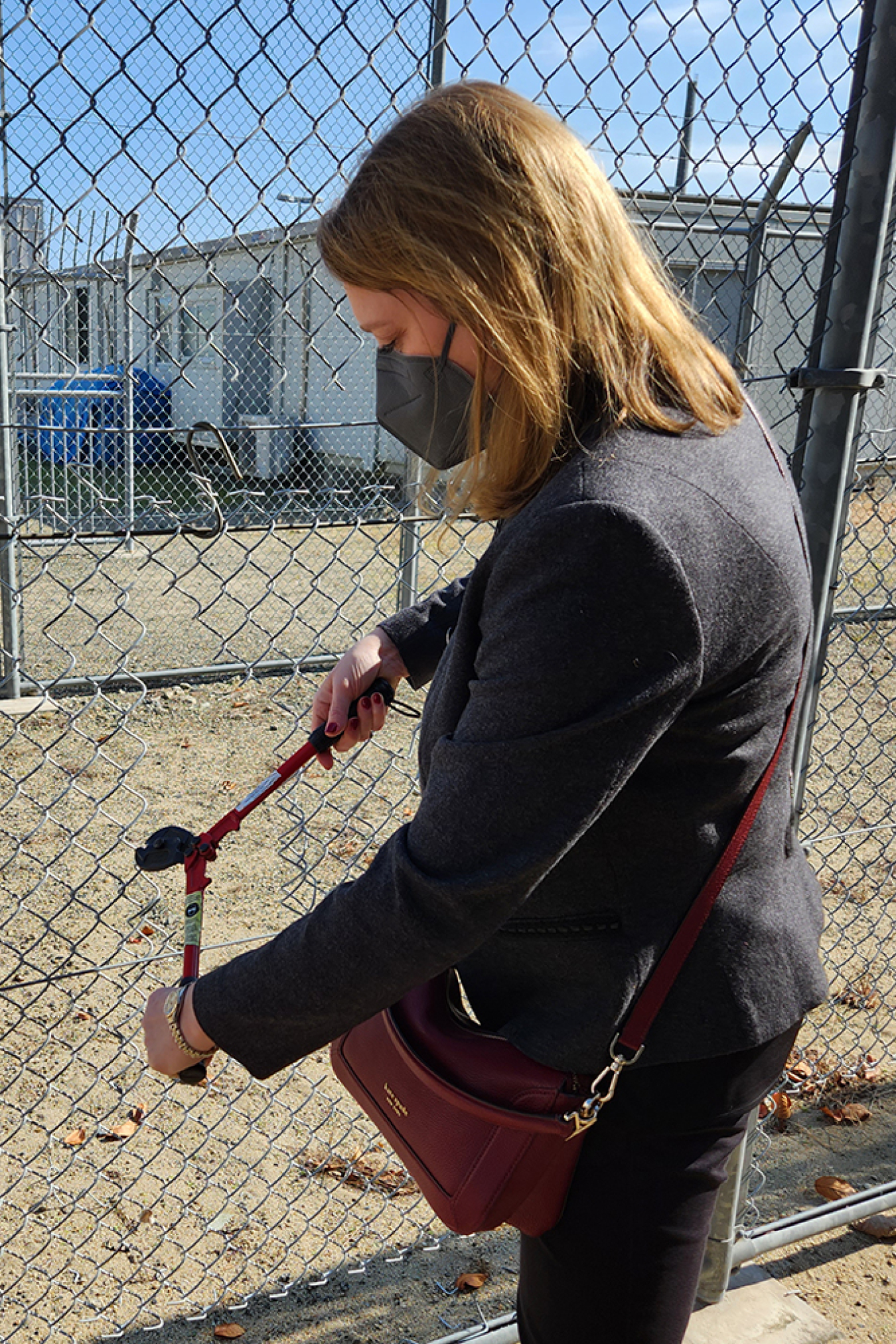 Corey Hinderstein uses bolt cutters to cut through a chain link fence.