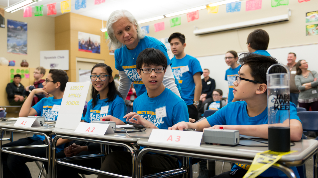 A student team of three prepares to compete in a National Science Bowl competition under the supervision of their teacher