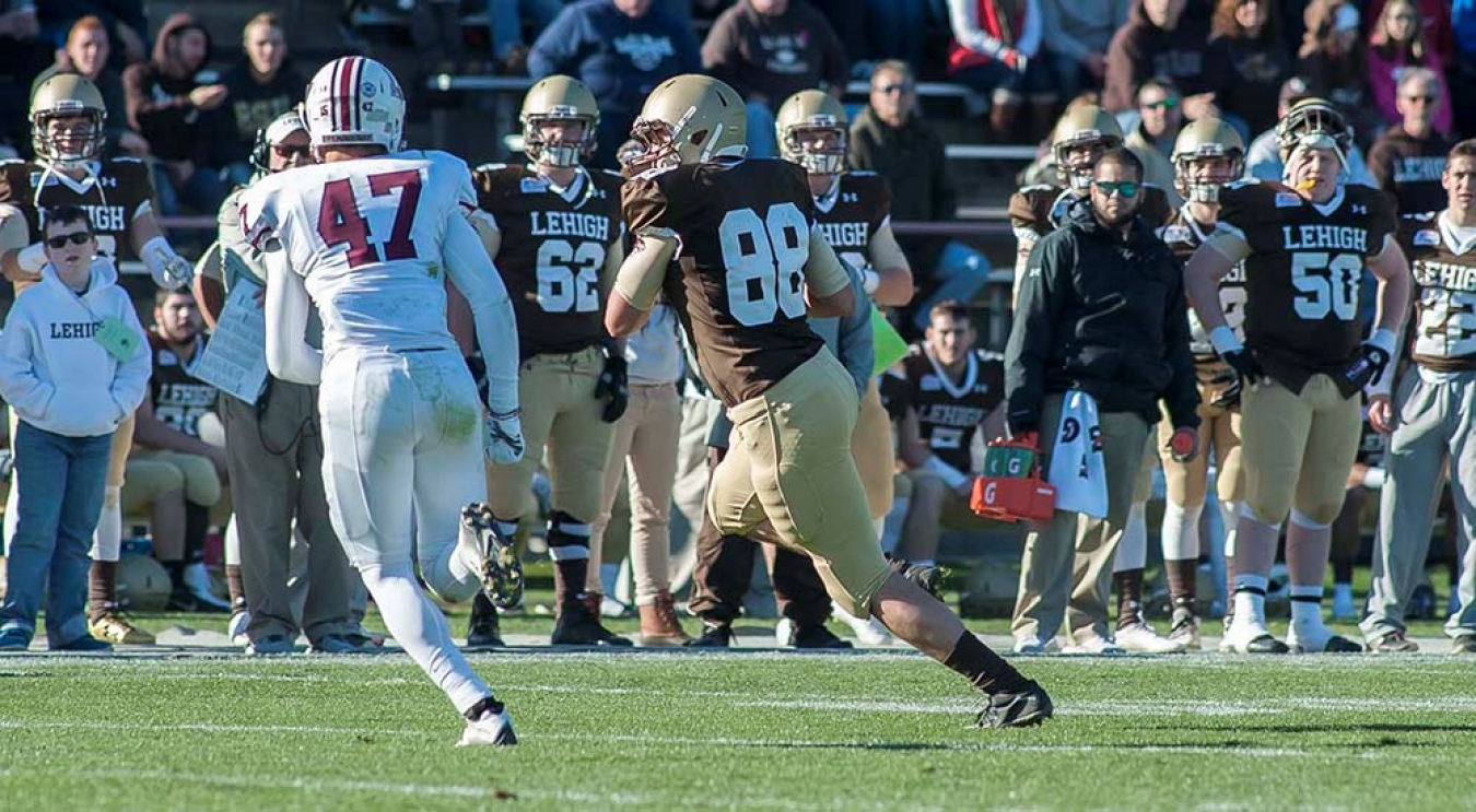 Two college-level football players from opposing teams run down the field during a game