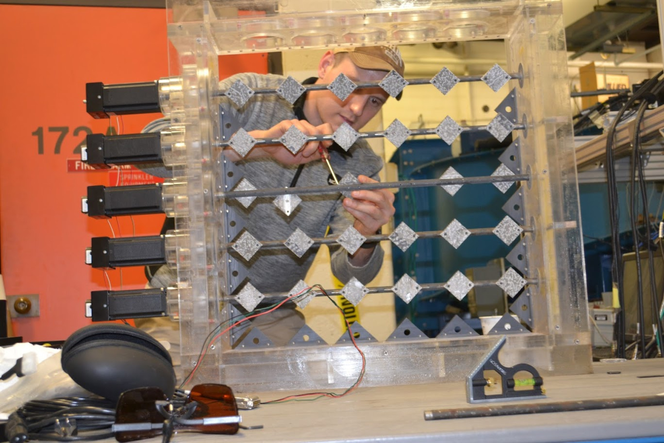 Christopher Ruhl works on an active grid turbulence generator, a square plastic frame containing metal slats.