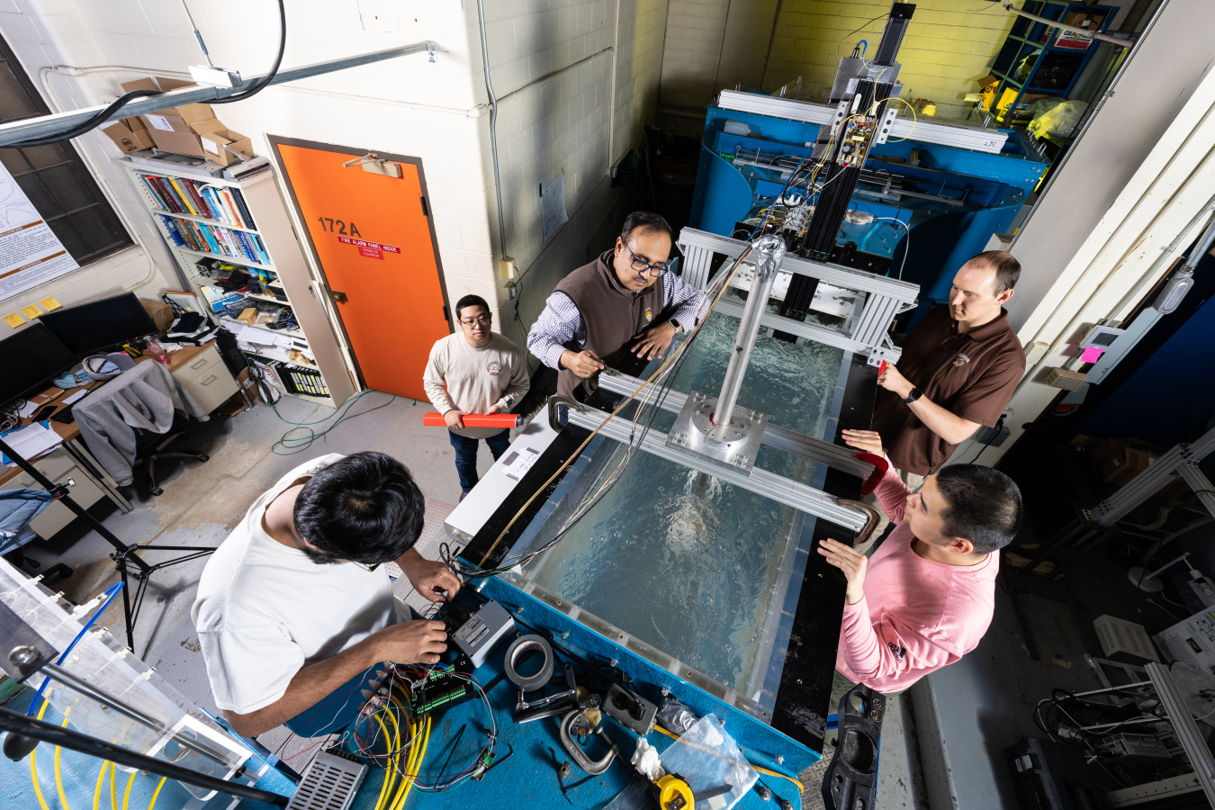 Five researchers look into rectangular tank filled with water, which has a tidal energy prototype submerged under water.