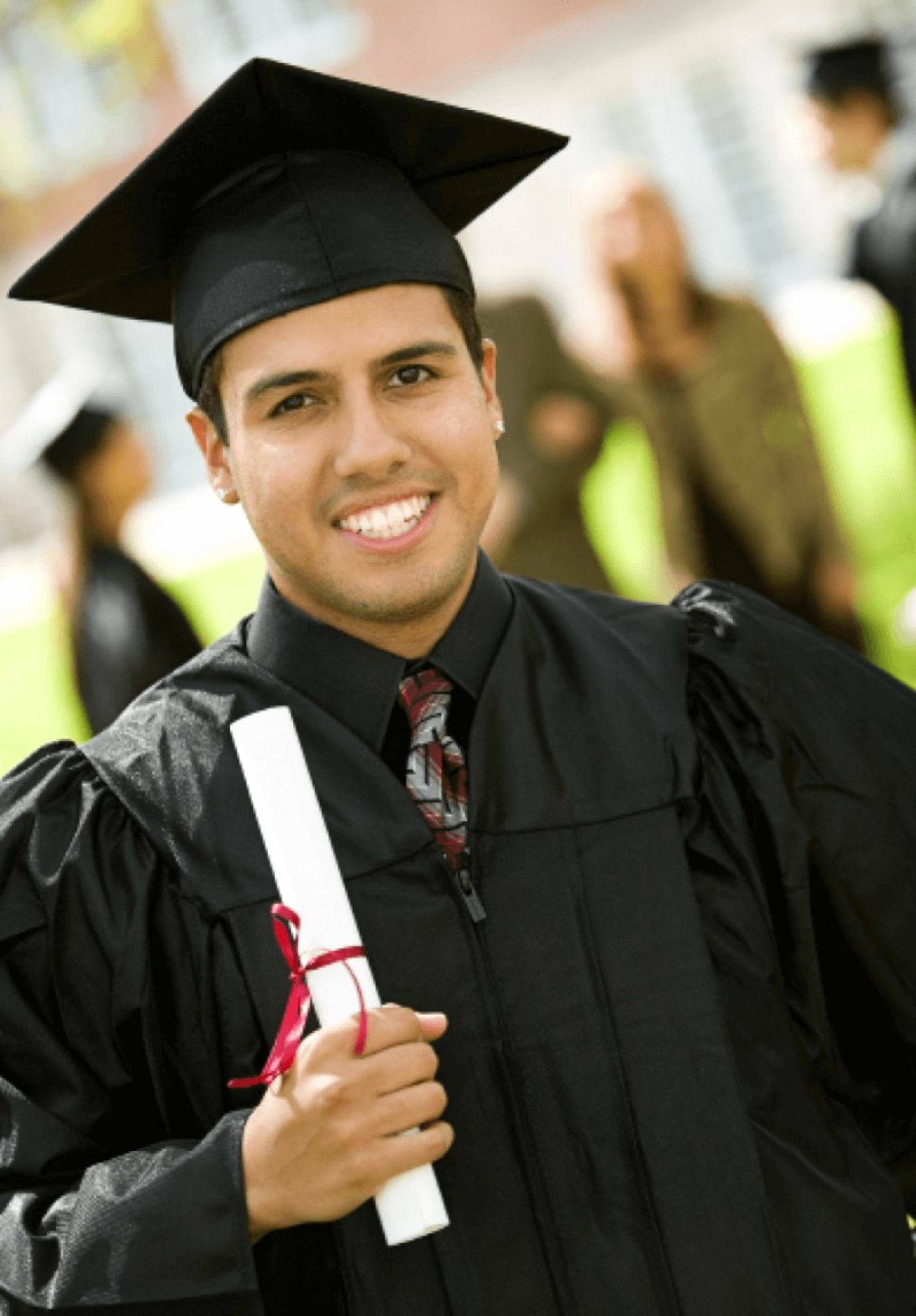 A Hispanic man in a cap and gown, holding a diploma